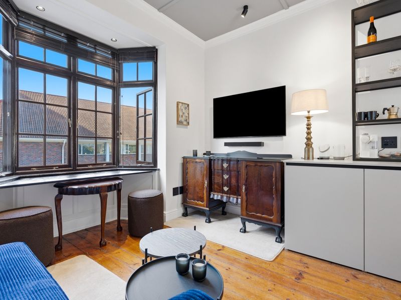 A well-maintained living room featuring polished timber flooring, a large bay window with dark frames, and built-in shelving units.