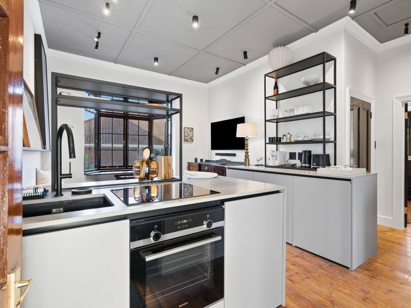 Modern kitchen featuring a sleek island with built-in oven and induction cooktop, matte black fixtures, coffered ceilings, and warm hardwood flooring.