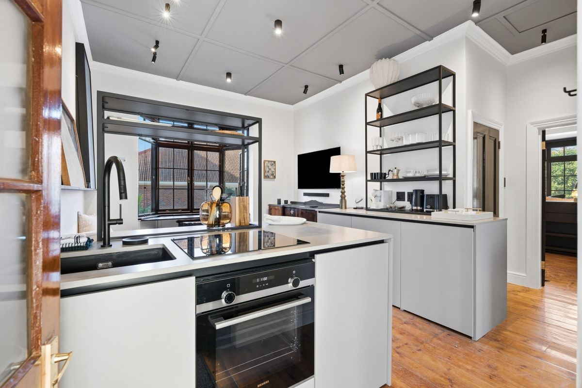 Modern kitchen featuring a sleek island with built-in oven and induction cooktop, matte black fixtures, coffered ceilings, and warm hardwood flooring.
