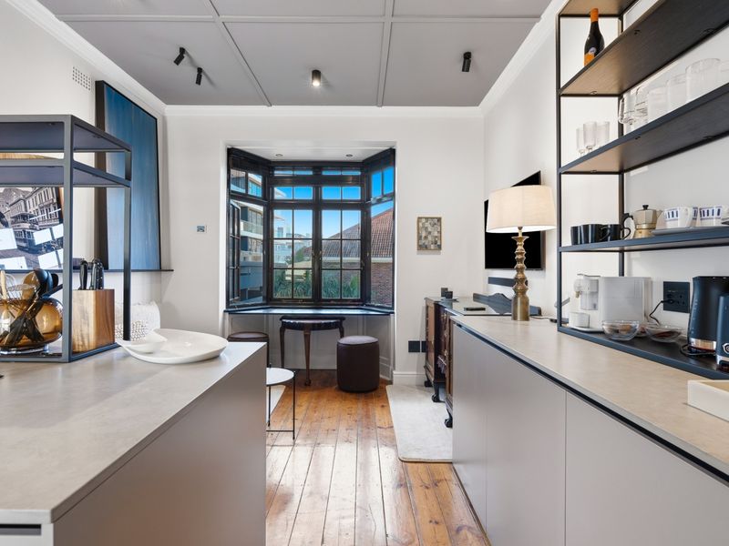 Modern kitchen featuring sleek cabinetry, stone countertops, hardwood flooring, and a charming bay window with natural light.