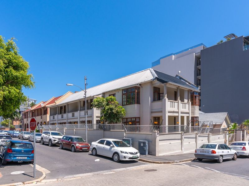 Street view of a multi-story apartment building featuring a metal roof, perimeter wall with electric fencing, and timber window frames.