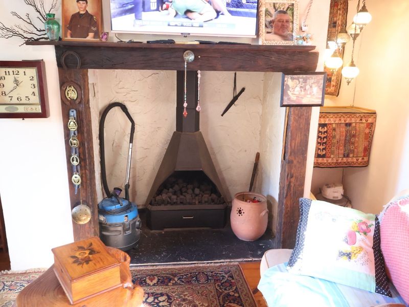 A rustic living room featuring a prominent built-in fireplace with a heavy timber mantle and a black metal firebox insert.