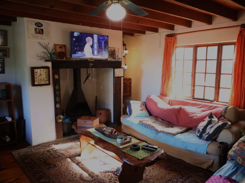 Cozy living room featuring exposed timber ceiling beams, a traditional fireplace with a wooden mantel, and large paneled windows allowing natural light.