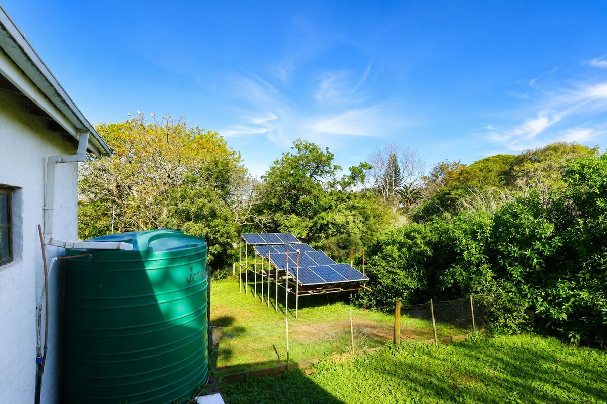 Rear garden area featuring a large green water storage tank and a ground-mounted solar panel array set within a lush, landscaped backyard.