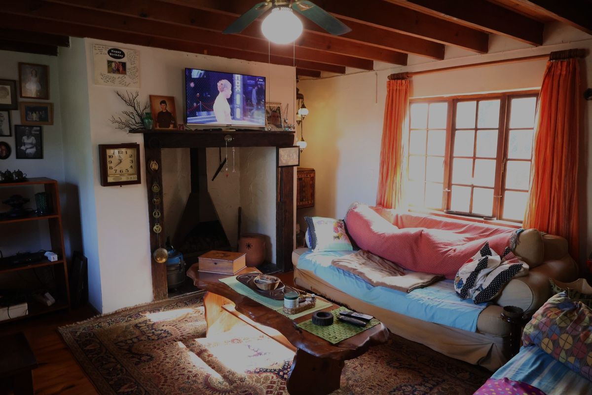 Cozy living room featuring exposed timber ceiling beams, a traditional fireplace with a wooden mantel, and large paneled windows allowing natural light.