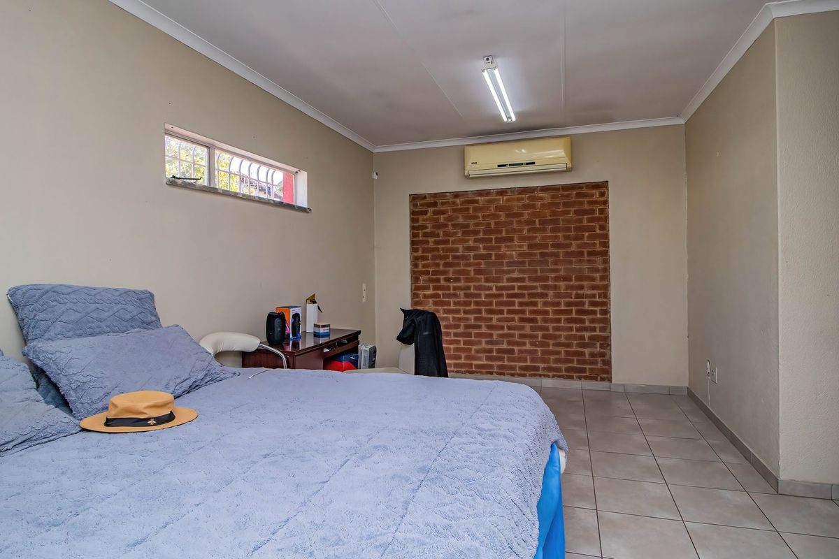 Bedroom featuring tiled flooring, an exposed brick feature wall, and a wall-mounted air conditioning unit.