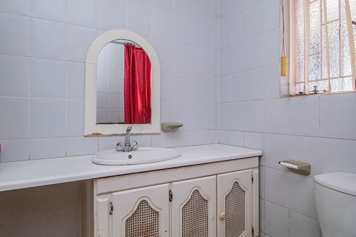 A dated bathroom featuring a vanity cabinet with basin, wall-mounted mirror, and ceramic wall tiling, requiring cosmetic updates to modernize the space.