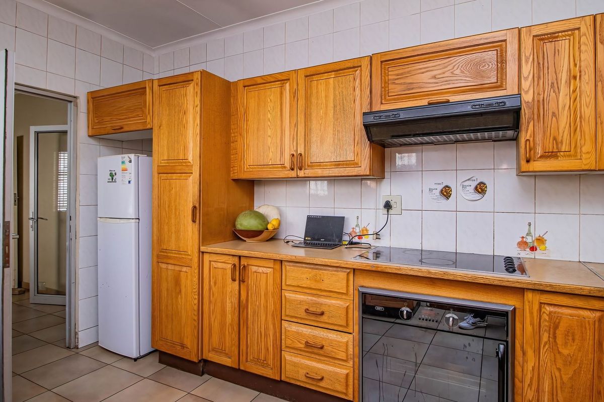 A functional kitchen featuring traditional wooden cabinetry, tiled backsplash, built-in oven, and electric cooktop with an integrated extractor fan.