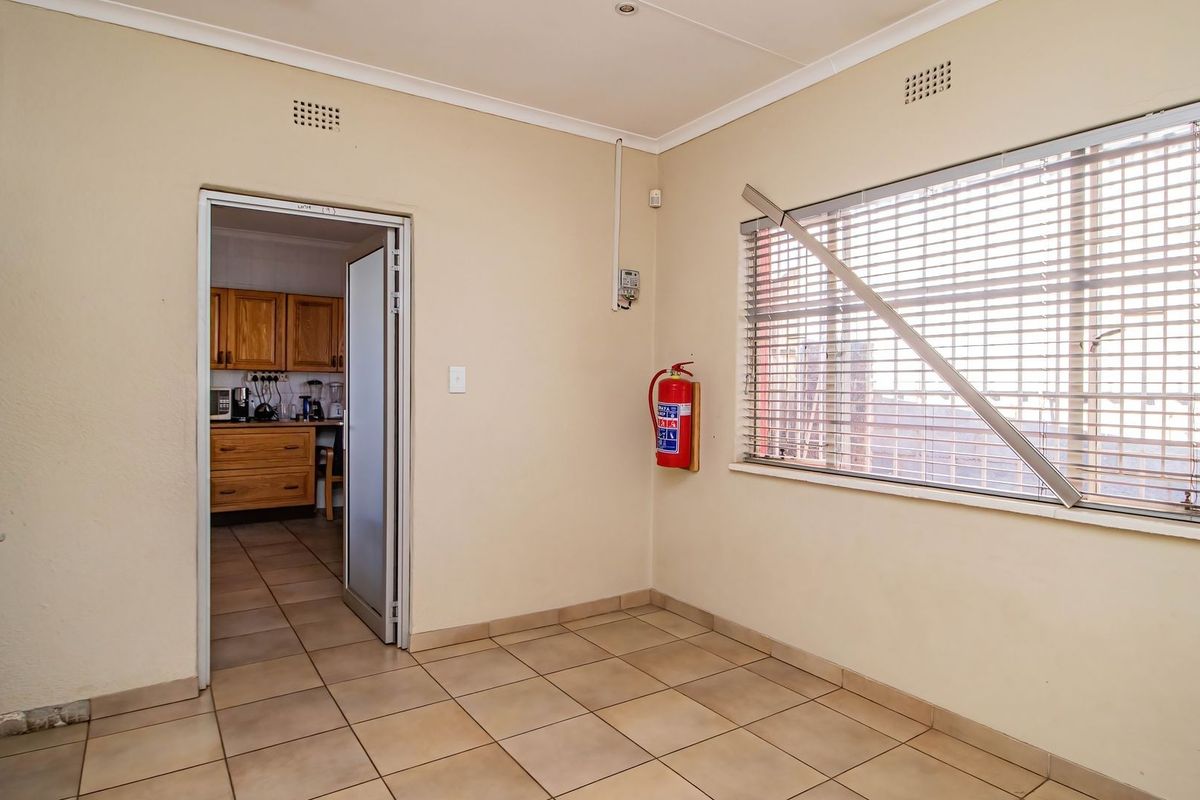 An empty living area featuring tiled flooring, coving, and a wall-mounted fire extinguisher, with a view into the adjacent kitchen.