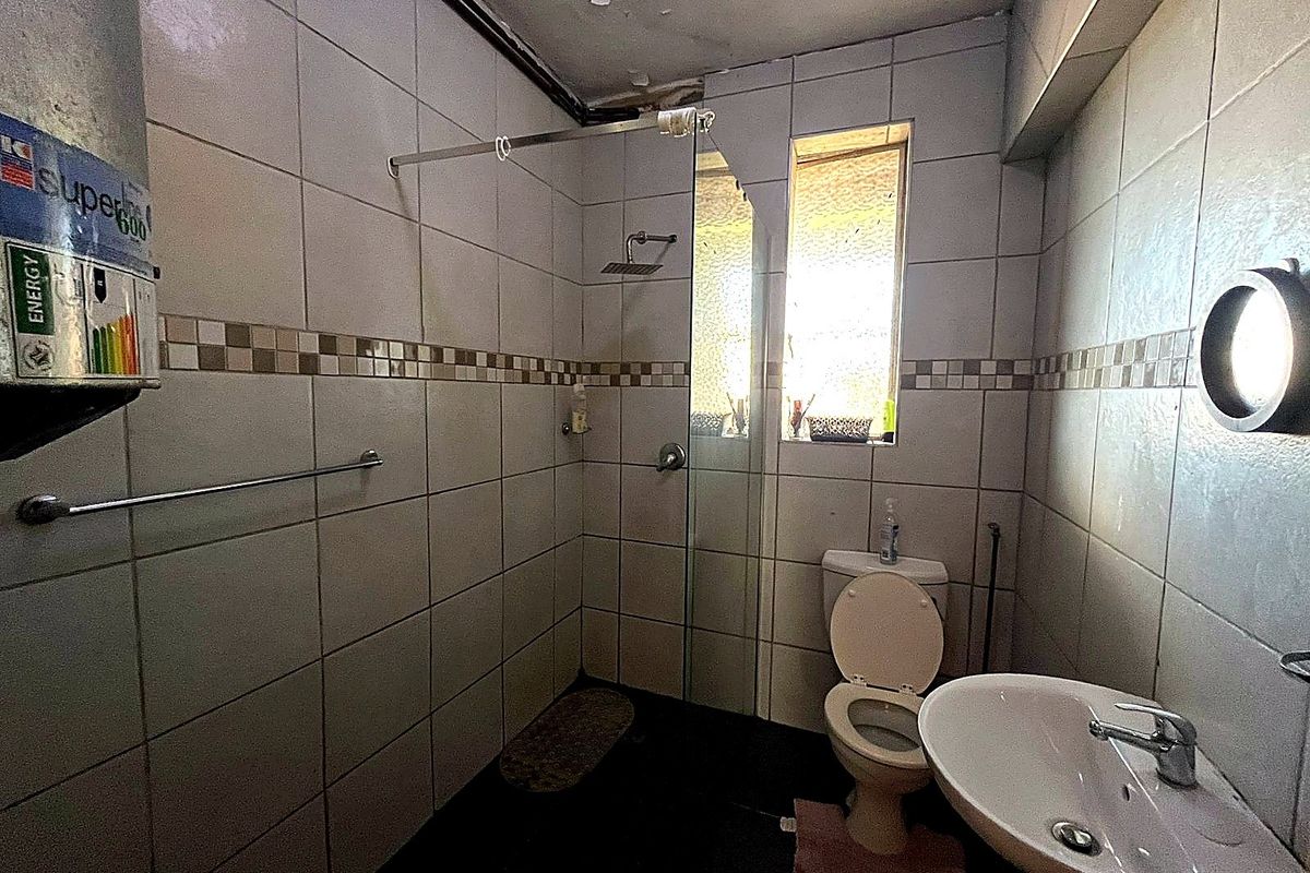 A dated bathroom featuring a walk-in shower, pedestal basin, and toilet, requiring significant maintenance and cosmetic updates to the ceiling and tiling.