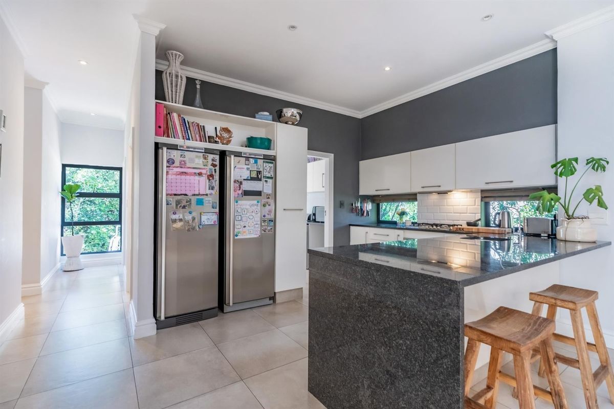 Modern kitchen featuring a granite breakfast bar, white cabinetry, subway tile backsplash, and recessed lighting, seamlessly flowing into an adjacent hallway.