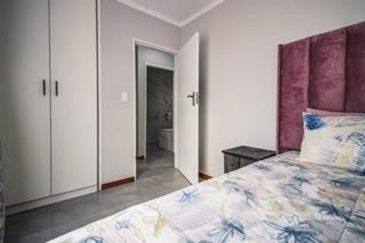 A well-maintained bedroom featuring built-in cupboards, tiled flooring, and direct access to an adjoining bathroom.