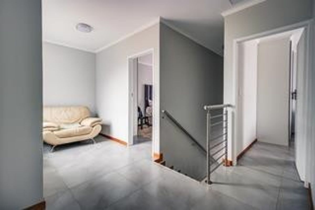 A bright landing area featuring tiled flooring, a modern metal staircase railing, and access to adjacent bedrooms.