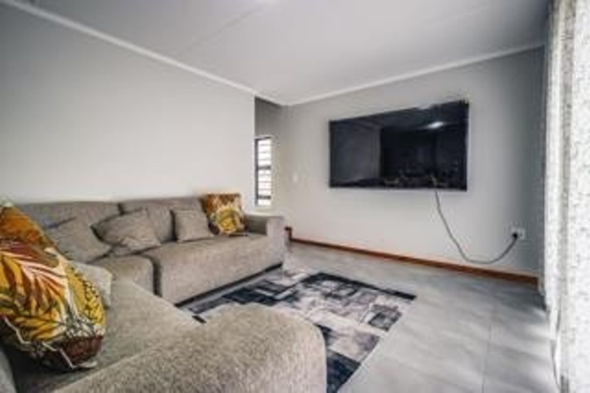 A bright living room featuring tiled flooring, neutral wall finishes, and a wall-mounted television setup.