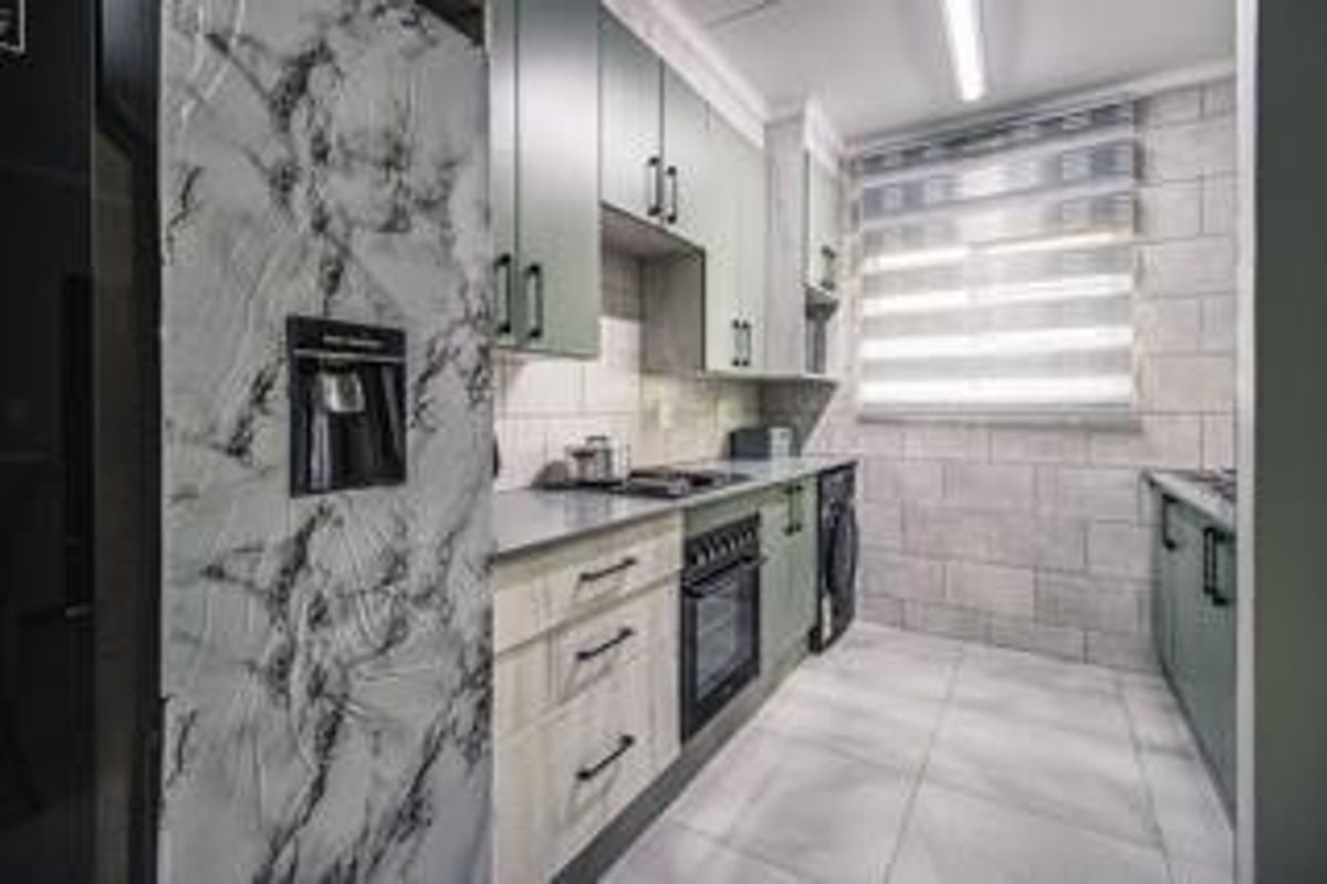 Modern kitchen featuring sage green cabinetry, stone-look countertops, built-in oven, and tiled flooring with a clean, contemporary aesthetic.