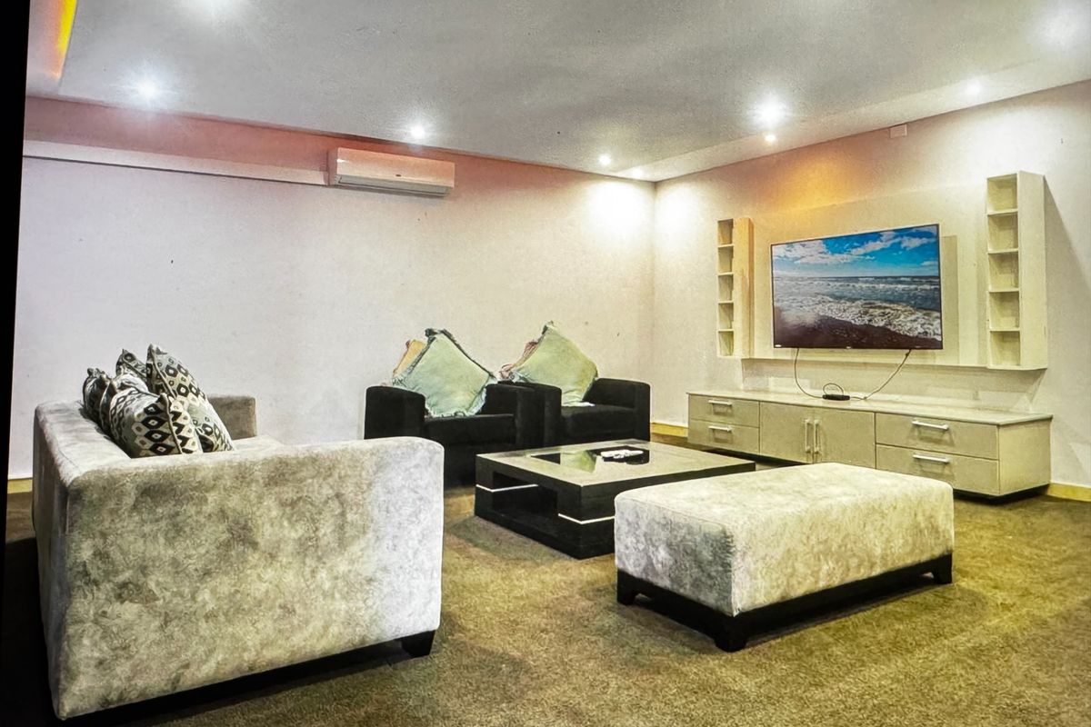 A spacious living room featuring recessed ceiling lighting, a wall-mounted air conditioning unit, and a custom built-in media console with integrated shelving.
