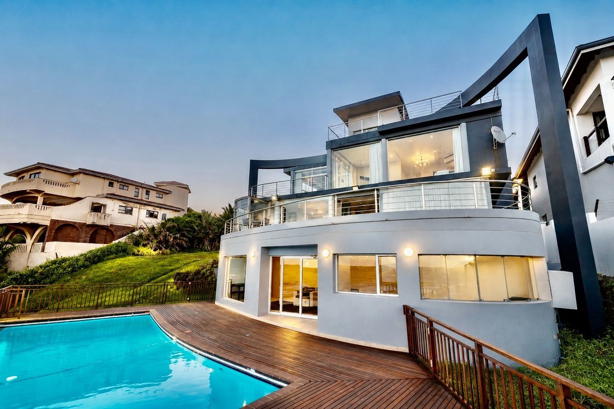 Modern multi-level residence featuring a curved architectural design, expansive glass windows, spacious balconies, and a timber deck surrounding a private swimming pool.
