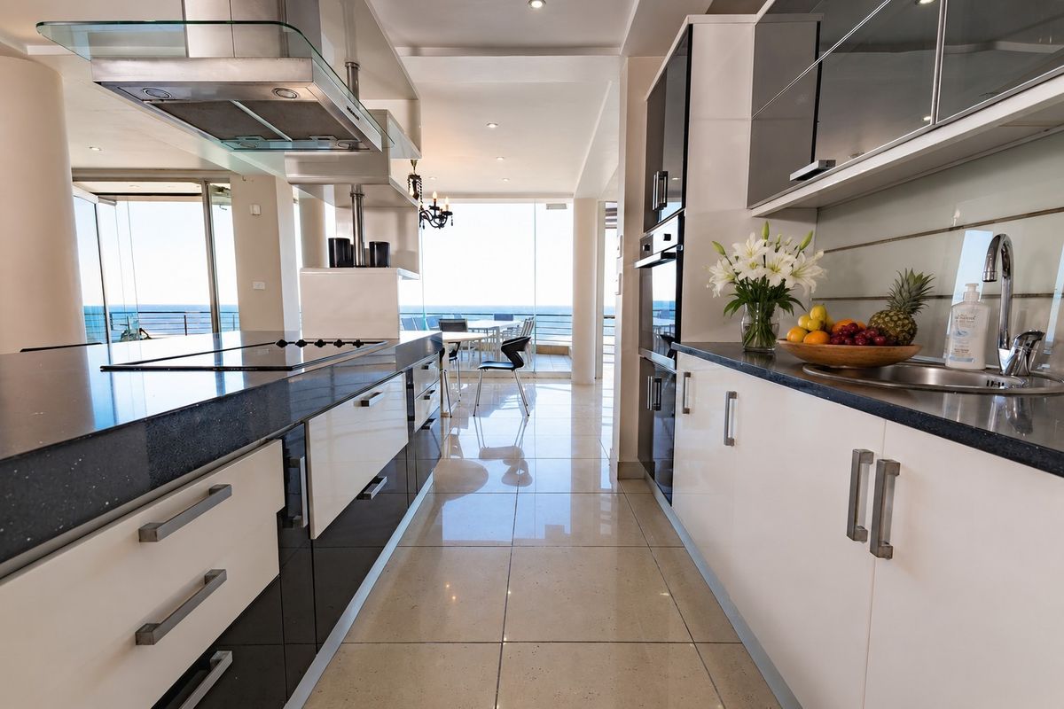 Modern kitchen featuring high-gloss cabinetry, stone countertops, built-in appliances, and a seamless flow toward an open-plan living area with ocean views.