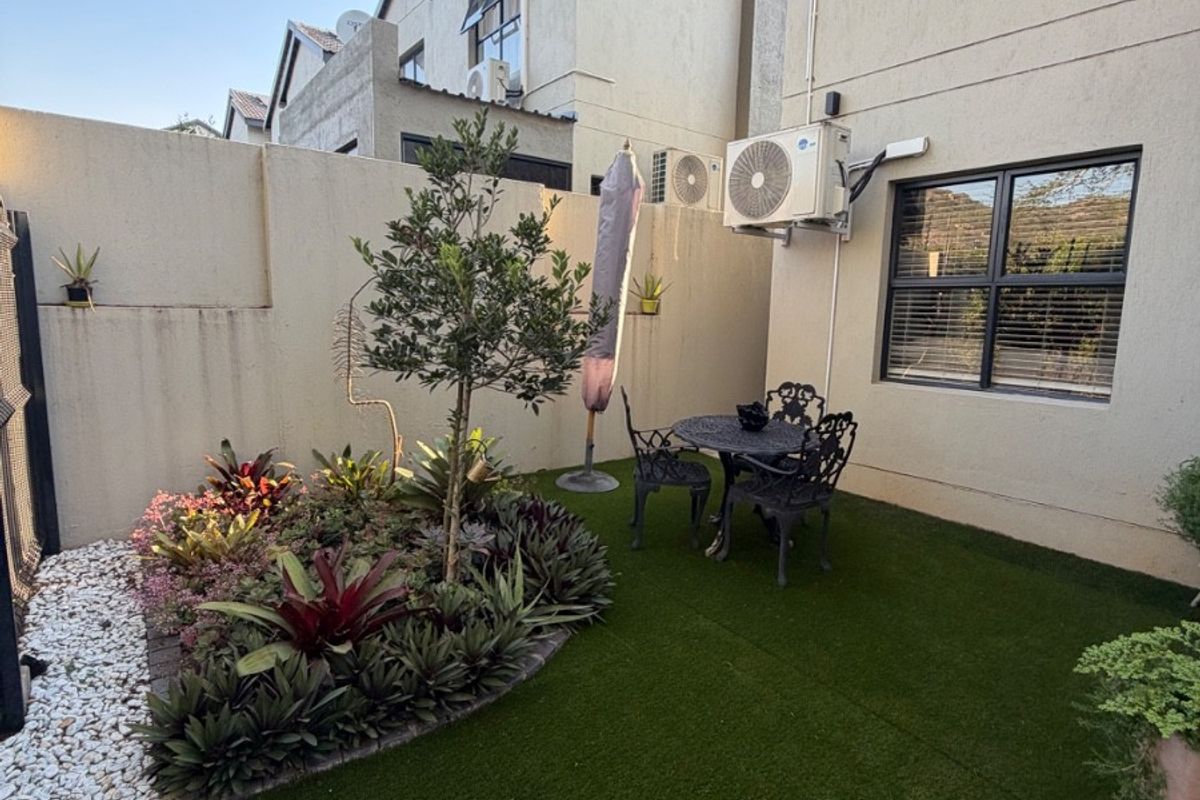 A private rear garden featuring artificial turf, a landscaped garden bed, and a paved border, adjacent to the exterior wall of the house.