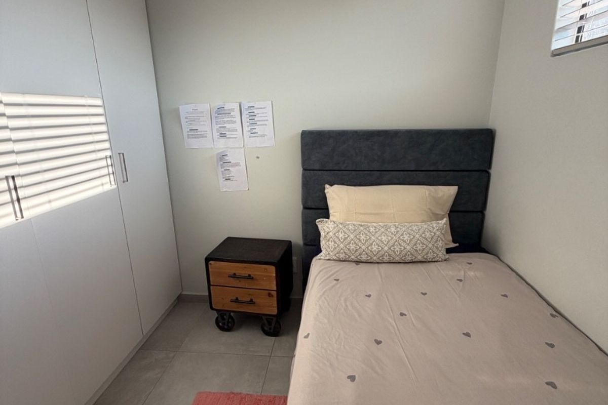 A compact bedroom featuring built-in floor-to-ceiling wardrobes, tiled flooring, and a wall-mounted air conditioning unit.