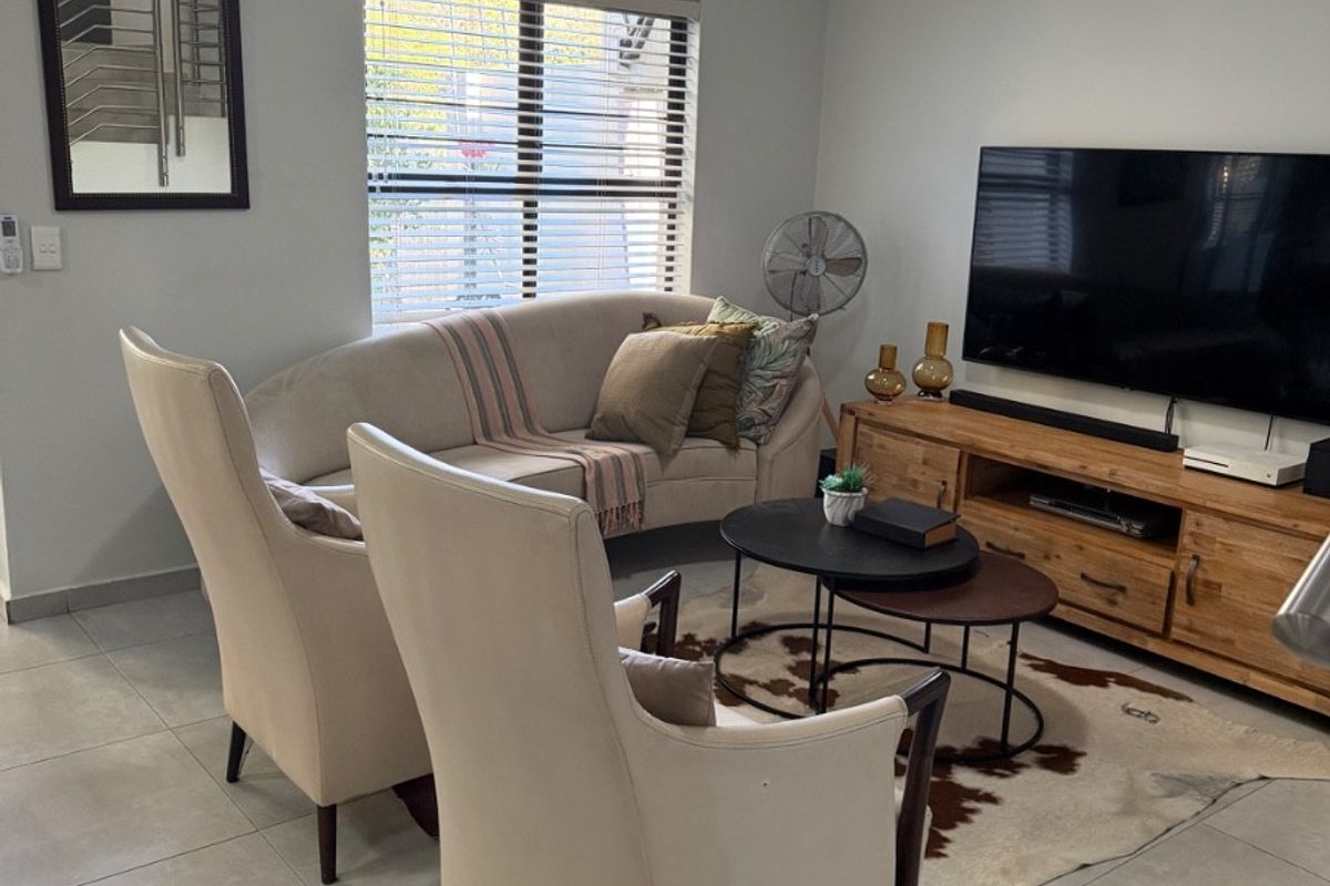 A comfortable living room featuring neutral floor tiles, a wall-mounted air conditioning unit, and large windows with fitted blinds.