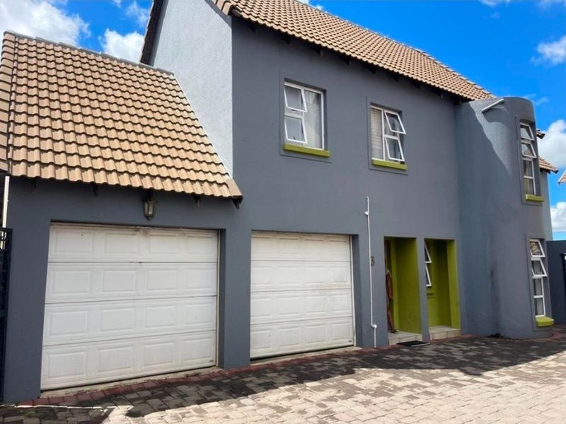 Front elevation of a double-story townhouse featuring a double garage, tiled roof, and modern grey and lime green exterior paint finish.