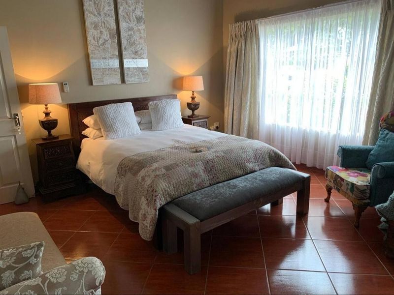 A comfortable bedroom featuring terracotta-style tiled flooring and large windows with curtain treatments, providing a warm and inviting atmosphere.