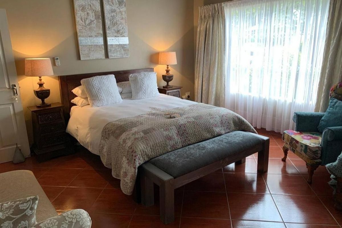 A comfortable bedroom featuring terracotta-style tiled flooring and large windows with curtain treatments, providing a warm and inviting atmosphere.