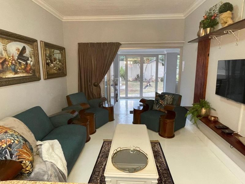 A comfortable living room featuring tiled flooring, coved ceilings, and large sliding glass doors that provide direct access to the rear garden area.