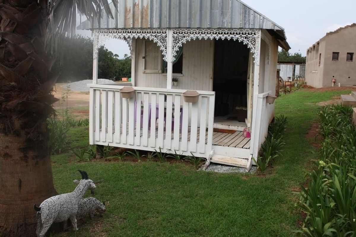 A small detached timber structure featuring a corrugated metal roof and decorative fretwork, set within a garden area.