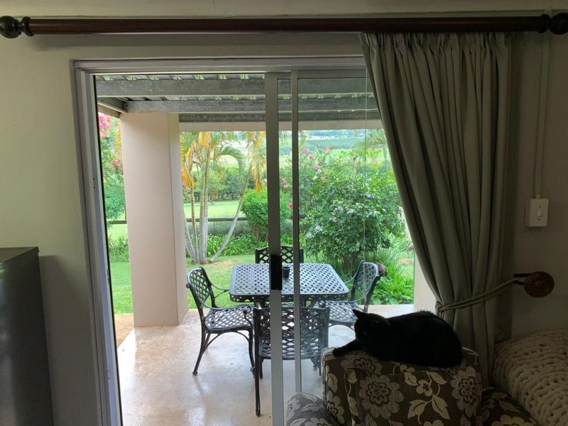 A covered patio area featuring concrete flooring and a sliding glass door, overlooking a lush garden landscape.