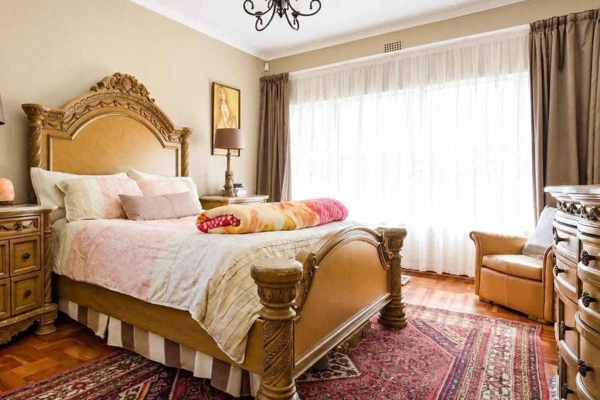 A well-lit bedroom featuring polished parquet flooring, large windows with curtains, and a classic chandelier.
