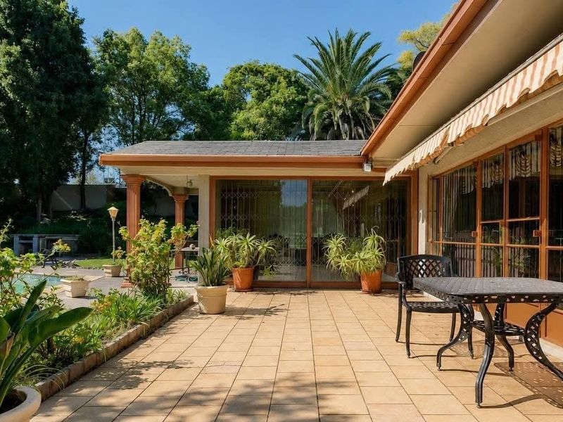 A spacious paved patio area featuring a retractable awning, sliding glass doors, and direct access to the garden and pool area.