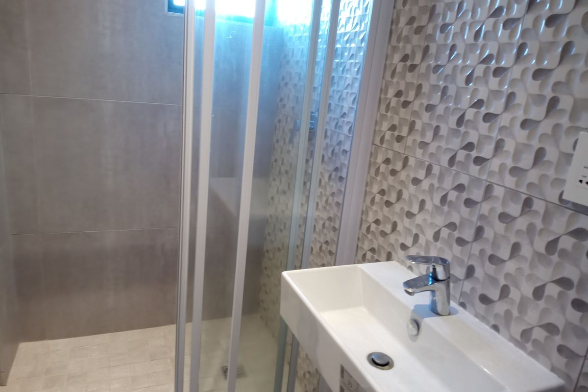 Modern bathroom featuring a wall-mounted basin with chrome mixer tap and a glass-enclosed shower with textured feature tiling.