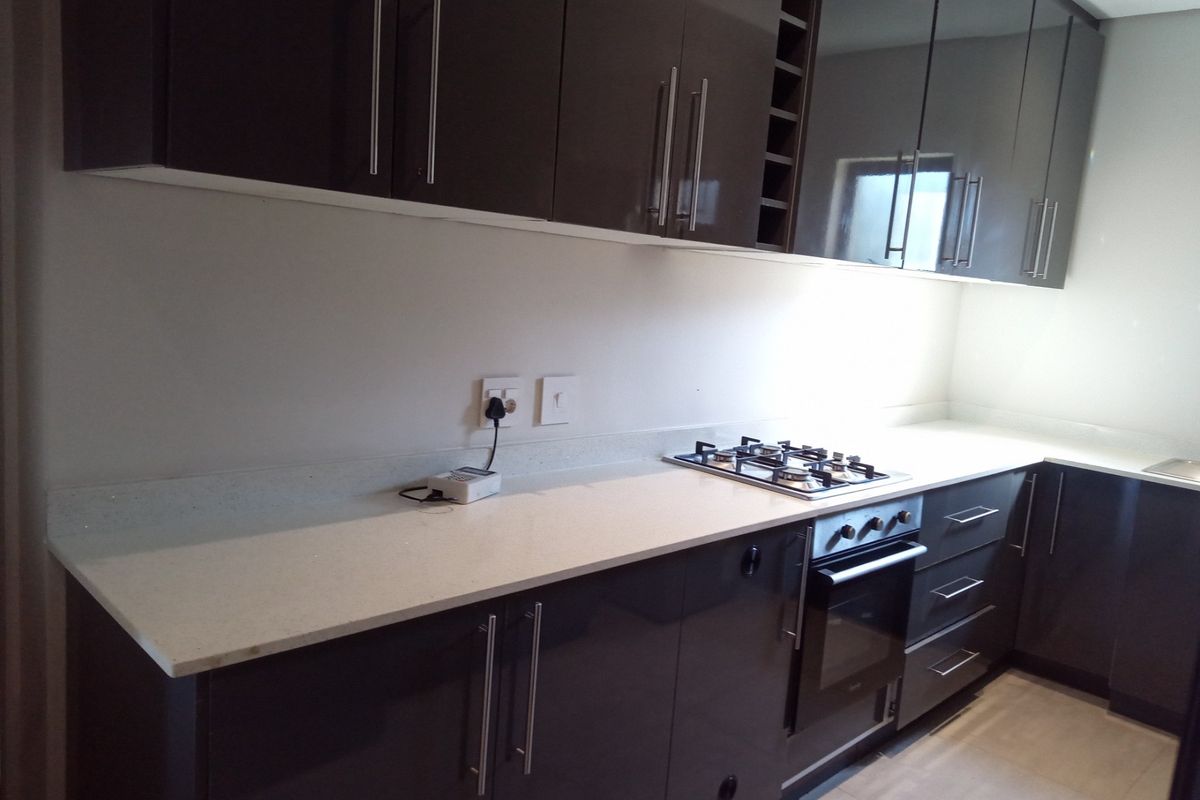 Modern kitchen featuring high-gloss dark cabinetry, stone countertops, a built-in oven, and a gas hob.