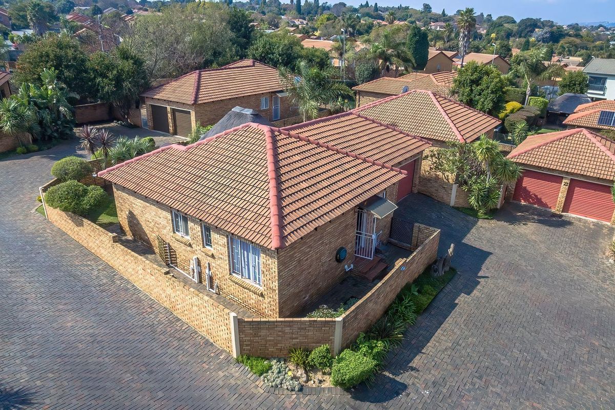 Aerial view of a brick townhouse complex featuring tiled roofs, paved driveways, and private walled garden areas.