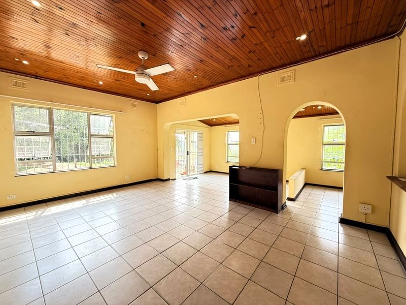 Spacious open-plan living area featuring a timber-clad ceiling, tiled flooring, and arched architectural details, offering a versatile layout with abundant natural light.