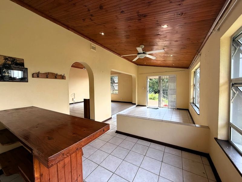 Spacious open-plan living area featuring a timber ceiling, built-in bar counter, tiled flooring, and direct access to the outdoor area through sliding glass doors.