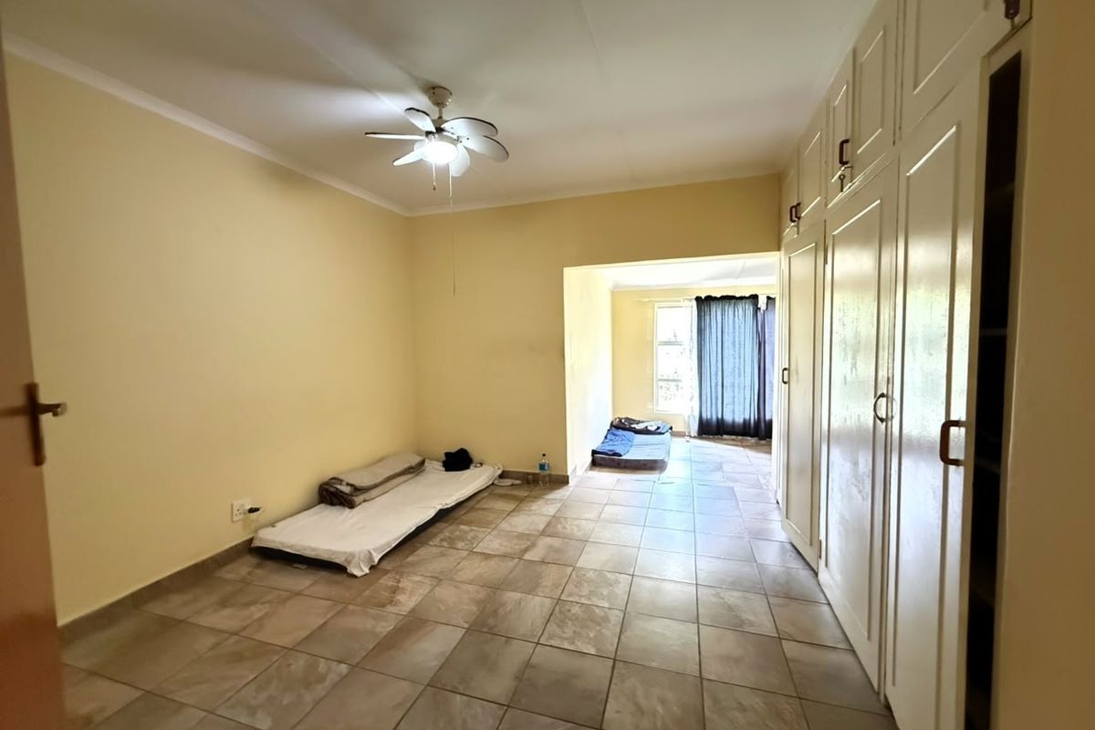 Spacious bedroom featuring tiled flooring, built-in cupboards, and a ceiling fan, offering a clean and functional layout.