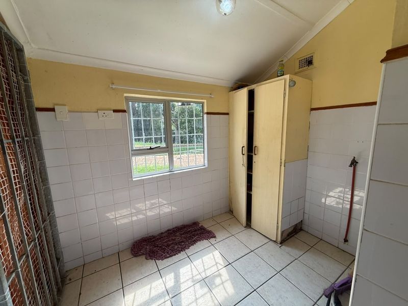 A functional laundry area featuring tiled walls and flooring, a built-in cupboard, and plumbing connections, ready for modernization or utility upgrades.