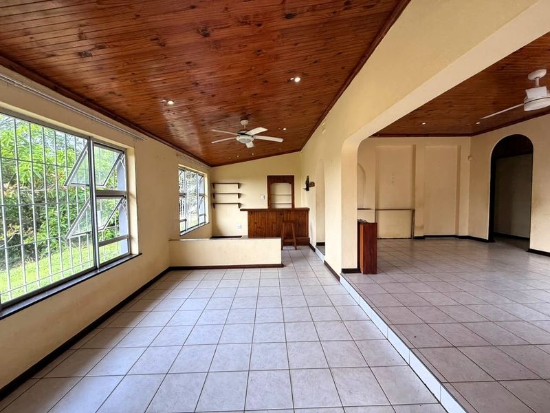 Spacious open-plan living area featuring a timber-clad ceiling, ceramic tiled flooring, and a built-in bar, offering a versatile layout for entertaining.