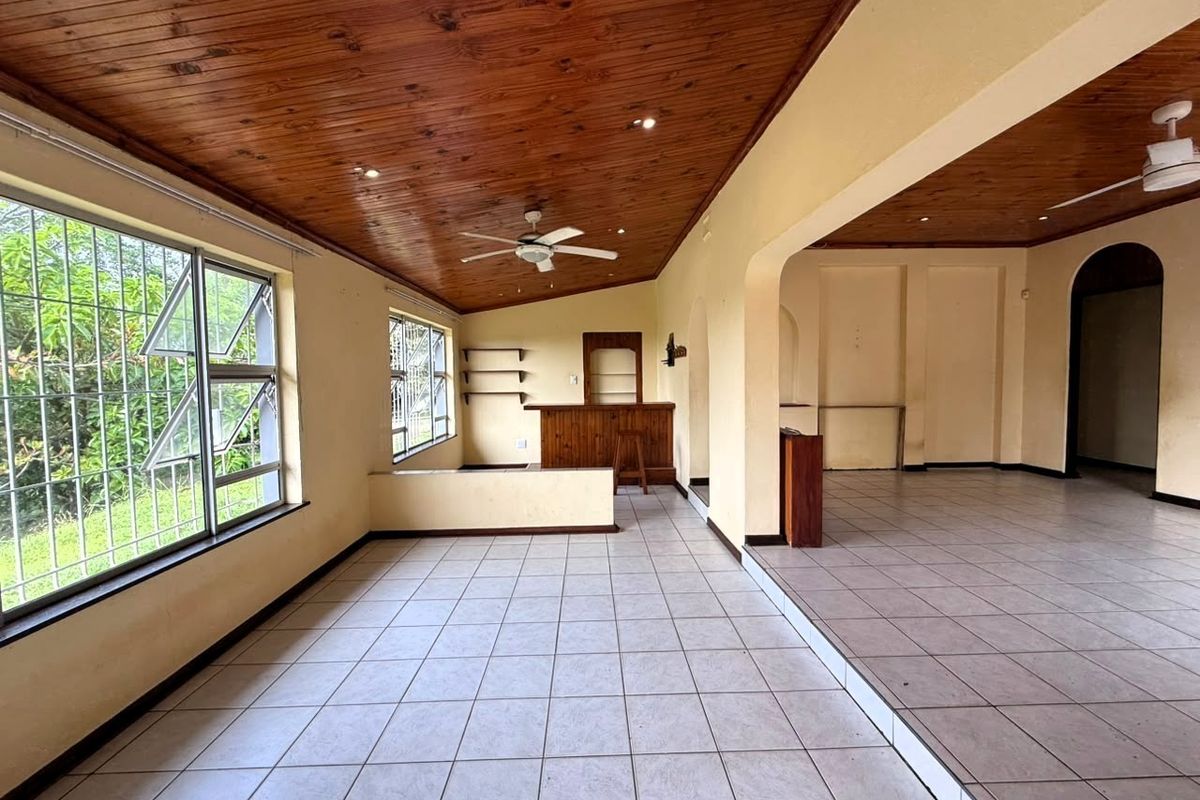 Spacious open-plan living area featuring a timber-clad ceiling, ceramic tiled flooring, and a built-in bar, offering a versatile layout for entertaining.