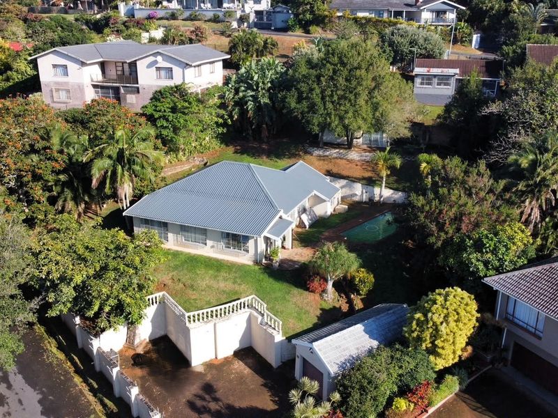 Aerial view of a residential property featuring a metal roof, swimming pool, detached garage, and established garden within a suburban neighborhood.