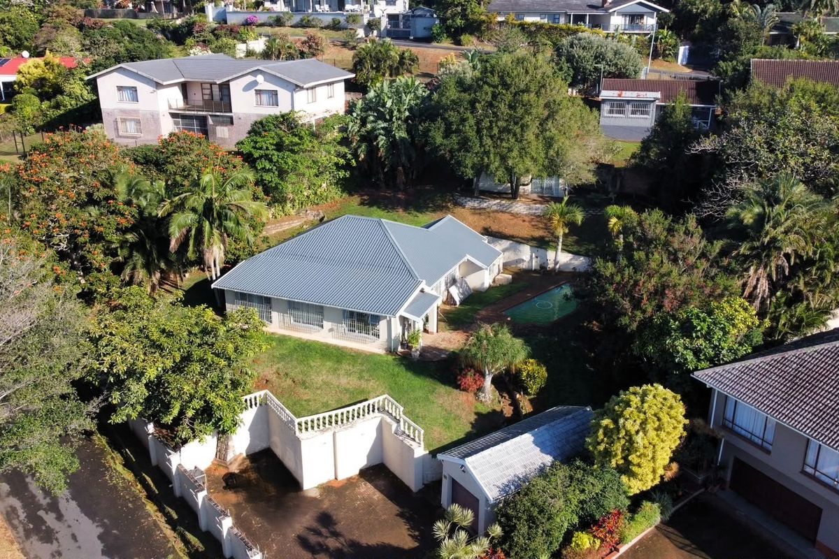 Aerial view of a residential property featuring a metal roof, swimming pool, detached garage, and established garden within a suburban neighborhood.