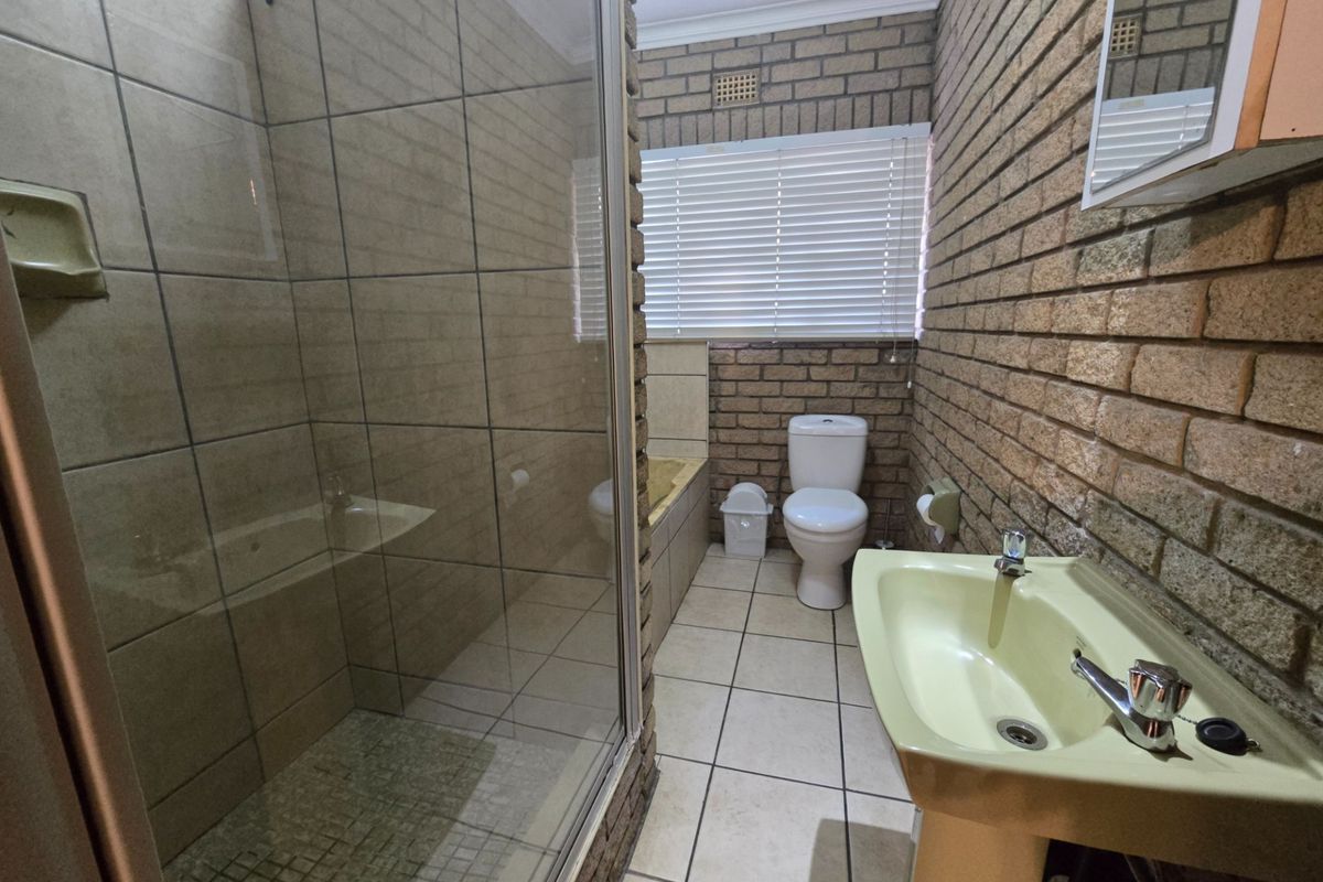 A dated bathroom featuring a glass-enclosed shower, a built-in bathtub, and a pedestal basin with exposed brick wall finishes.