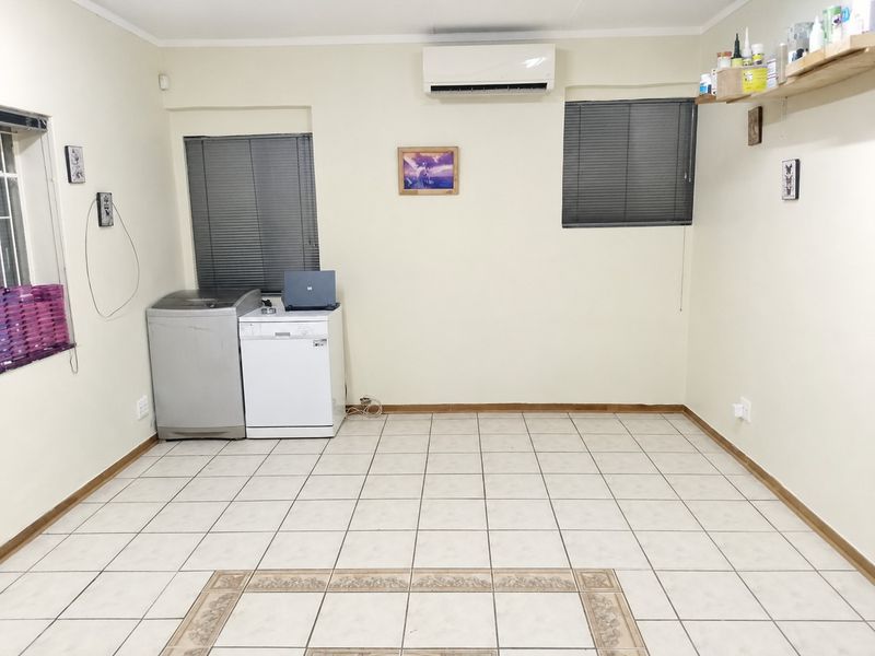 A functional laundry room featuring tiled flooring, wall-mounted air conditioning, and practical window blinds, offering a clean and versatile utility space.