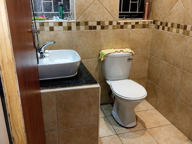A compact bathroom featuring a vessel sink on a granite vanity, a standard toilet, and full-height wall tiling with a decorative border.