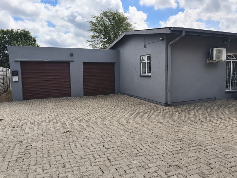 Front exterior view of the property featuring a paved driveway, double garage with roller shutter doors, and exterior air conditioning unit.
