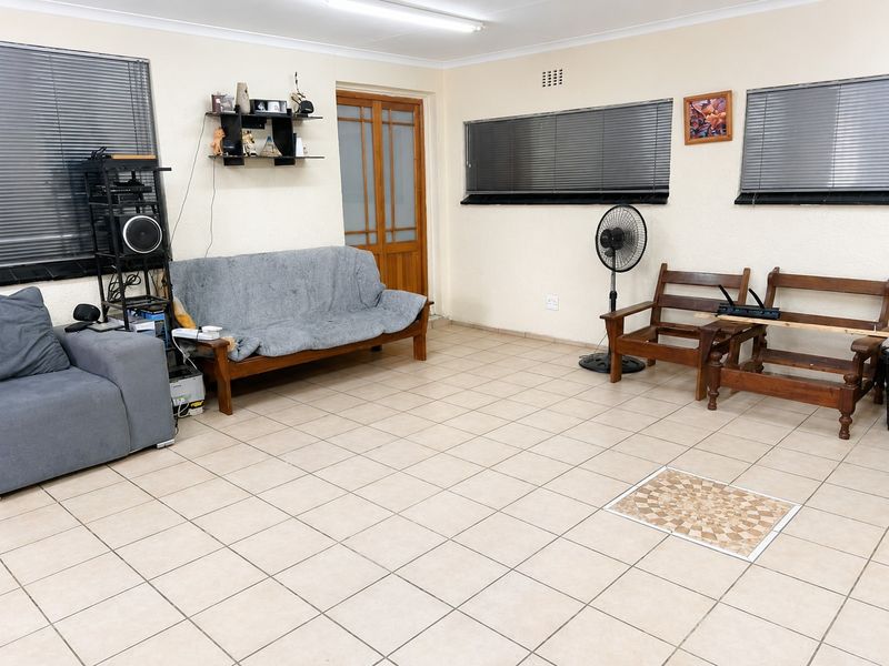 A spacious living area featuring neutral tiled flooring, venetian blinds, and a timber-framed door, offering a functional space ready for modern updates.