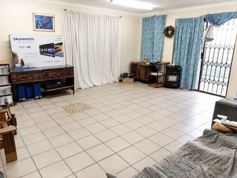 A spacious living area featuring neutral ceramic floor tiles, a sliding glass door with security gate, and simple coved cornicing.